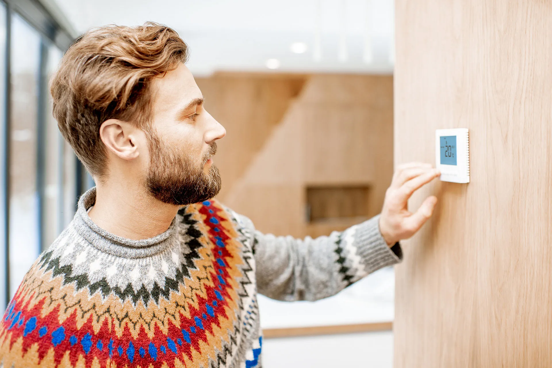 In einem modernen Wohnraum mit Holzoptik bedient ein Mann einen Thermostat zur Steuerung der Klimaanlage.