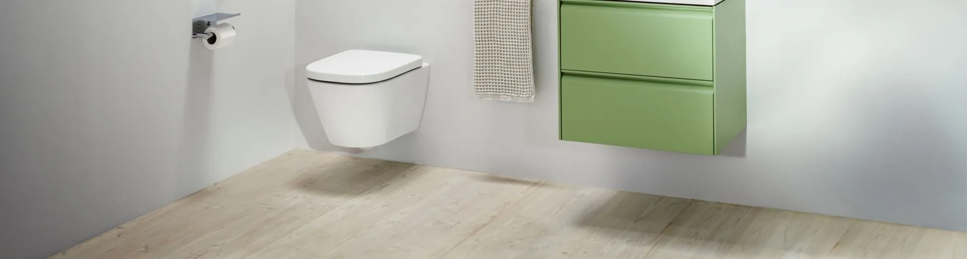 Ein kompaktes Badezimmer mit einem wandmontierten WC und einem grün lackierten Waschtisch mit zwei Schubladen.