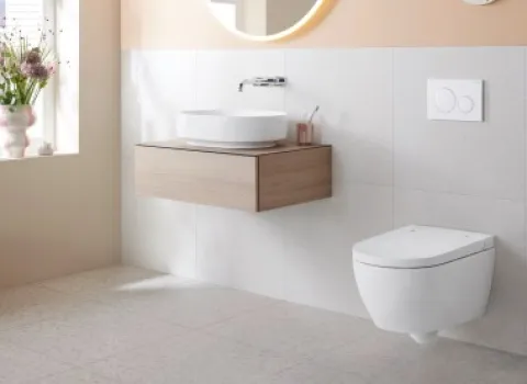 Helles Badezimmer mit dem Dusch-WC Geberit AquaClean Alba und einem schwebenden Holz-Waschtisch. Runde Spiegel und pastellfarbene Wandgestaltung.