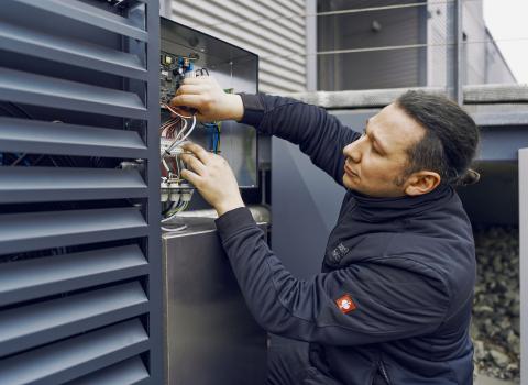 Ein Techniker überprüft eine Elektroinstallation an einer Außeneinheit, während er sorgfältig Kabel in einem offenen Schaltkasten anschließt.