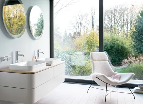 Badezimmer mit doppel Waschtisch, Sessel und bodentiefen Fenstern.