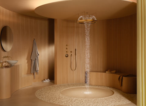 Ein modernes Badezimmer mit einer luxuriösen goldenen Regendusche, die Wasser in einem sanften Strom auf einen runden Kieselsteinboden fließen lässt. 