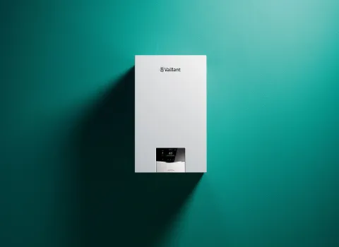 Weiße Heiztherme von Vaillant vor türkisfarbener Wand, mit schlichter Bauform und digitalem Display für Temperaturregelung.