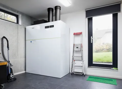Eine große Vaillant-Wärmepumpe steht in einem modern gestalteten Technikraum mit grauem Boden und einer großen Fensterfront, die den Blick ins Freie ermöglicht.