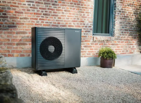 Eine moderne Vaillant-Wärmepumpe steht vor einem Backstein-Altbau.