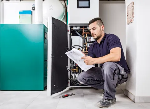 Ein Anlagenmechaniker SHK wartet eine Heizung mit Checkliste in der Hand.