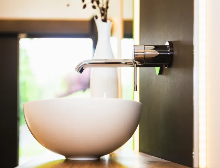 Ein modernes Badezimmer mit einer eleganten, weißen Aufsatz-Waschschüssel und einer wandmontierten Armatur aus glänzendem Chrom. 